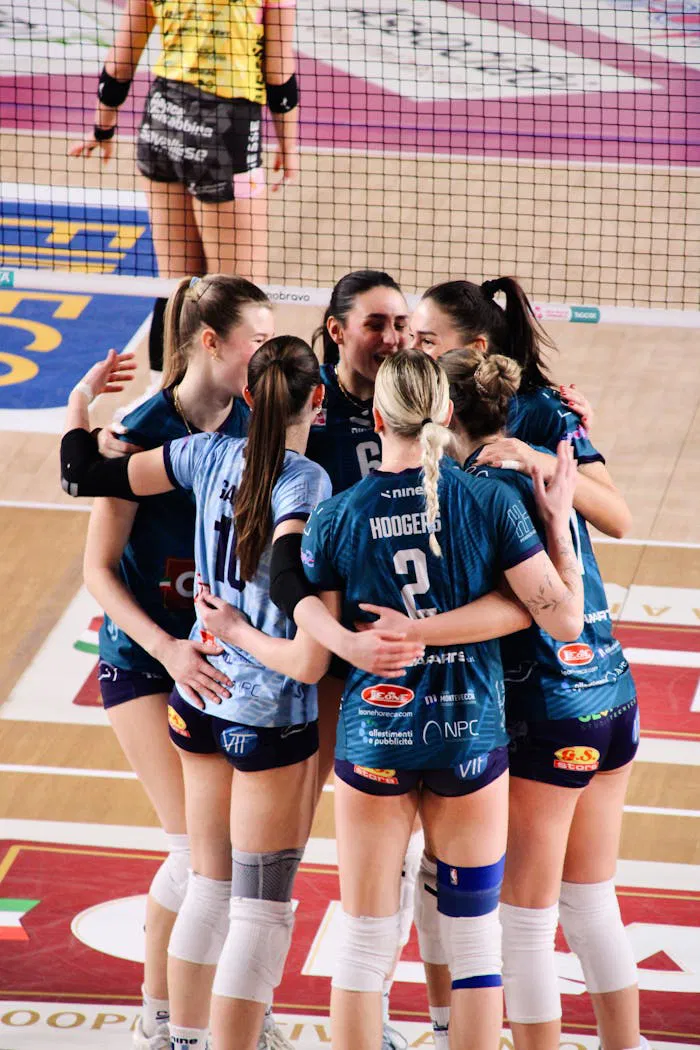 A group of female volleyball players celebrate on the court after scoring a point.