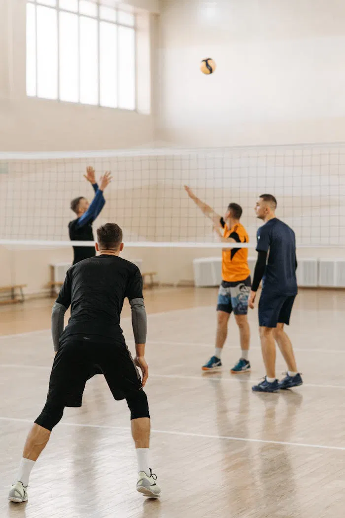 Four men engaged in an indoor volleyball game, showcasing athletic teamwork and lively competition.