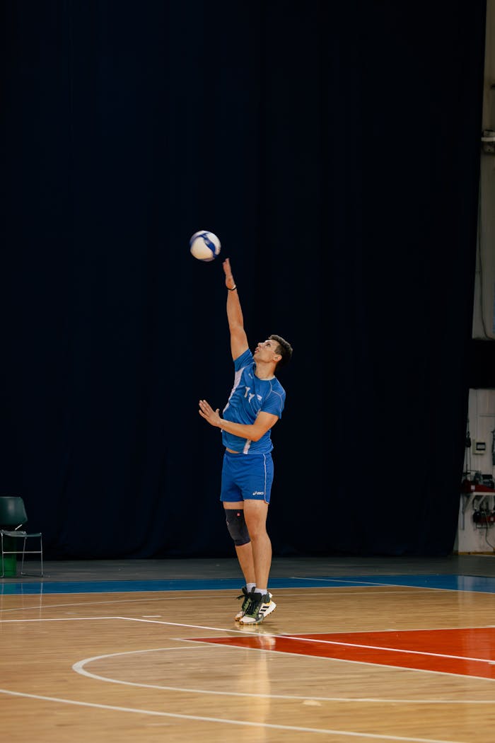 Athlete in blue kit performing a powerful serve in an indoor volleyball court.