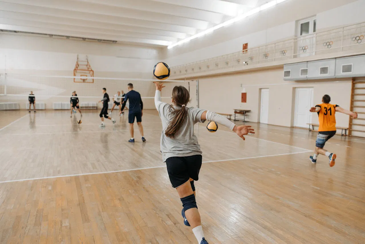 Coed volleyball team practicing indoors, focusing on teamwork and skill development.